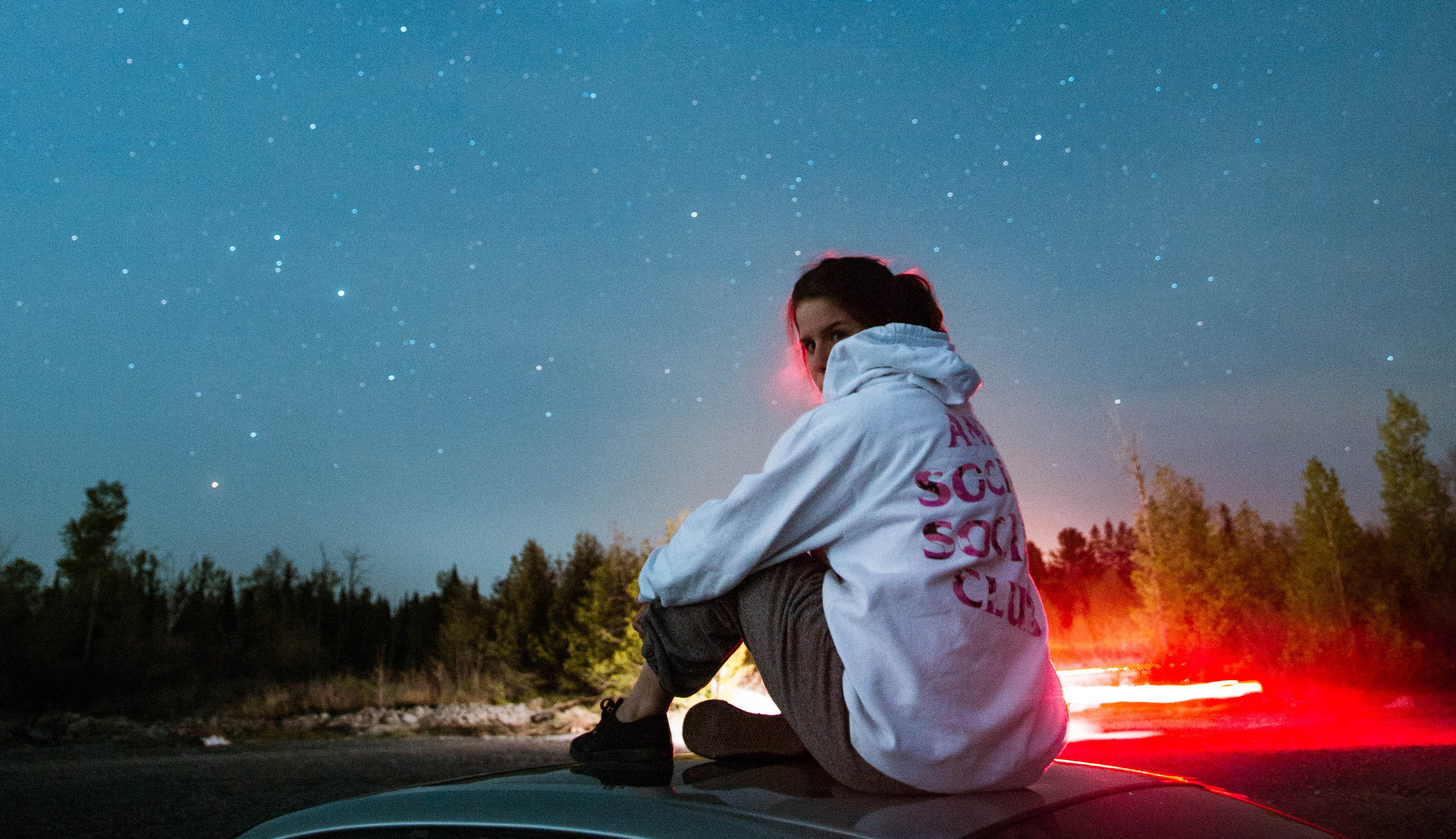jonge vrouw zit op motorkap met de sterrenhemel achter haar
