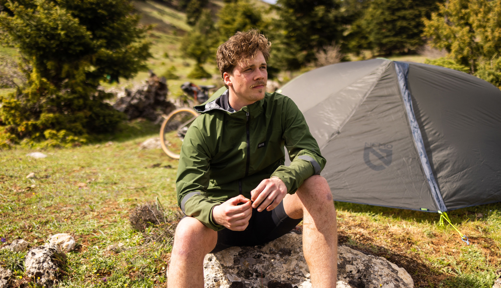 Iemand is aan het bikepacken en zit op een steen voor zijn tent.