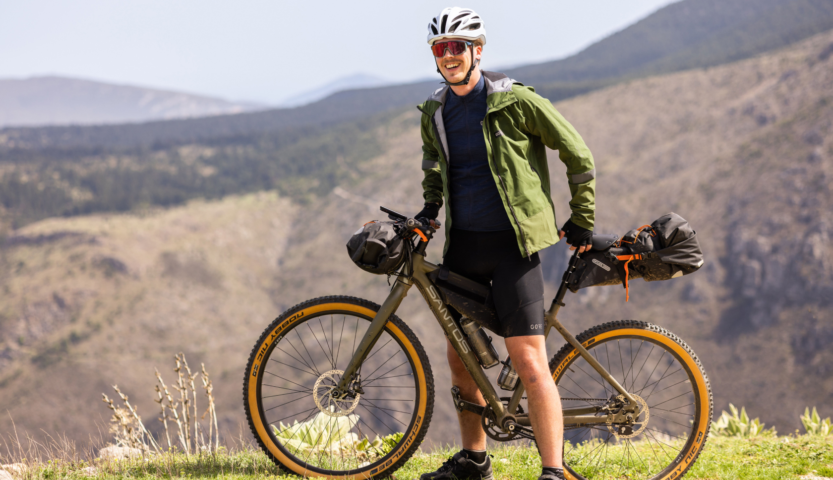 Een bikepacker staat in fietskleding voor zijn fiets in de bergen.