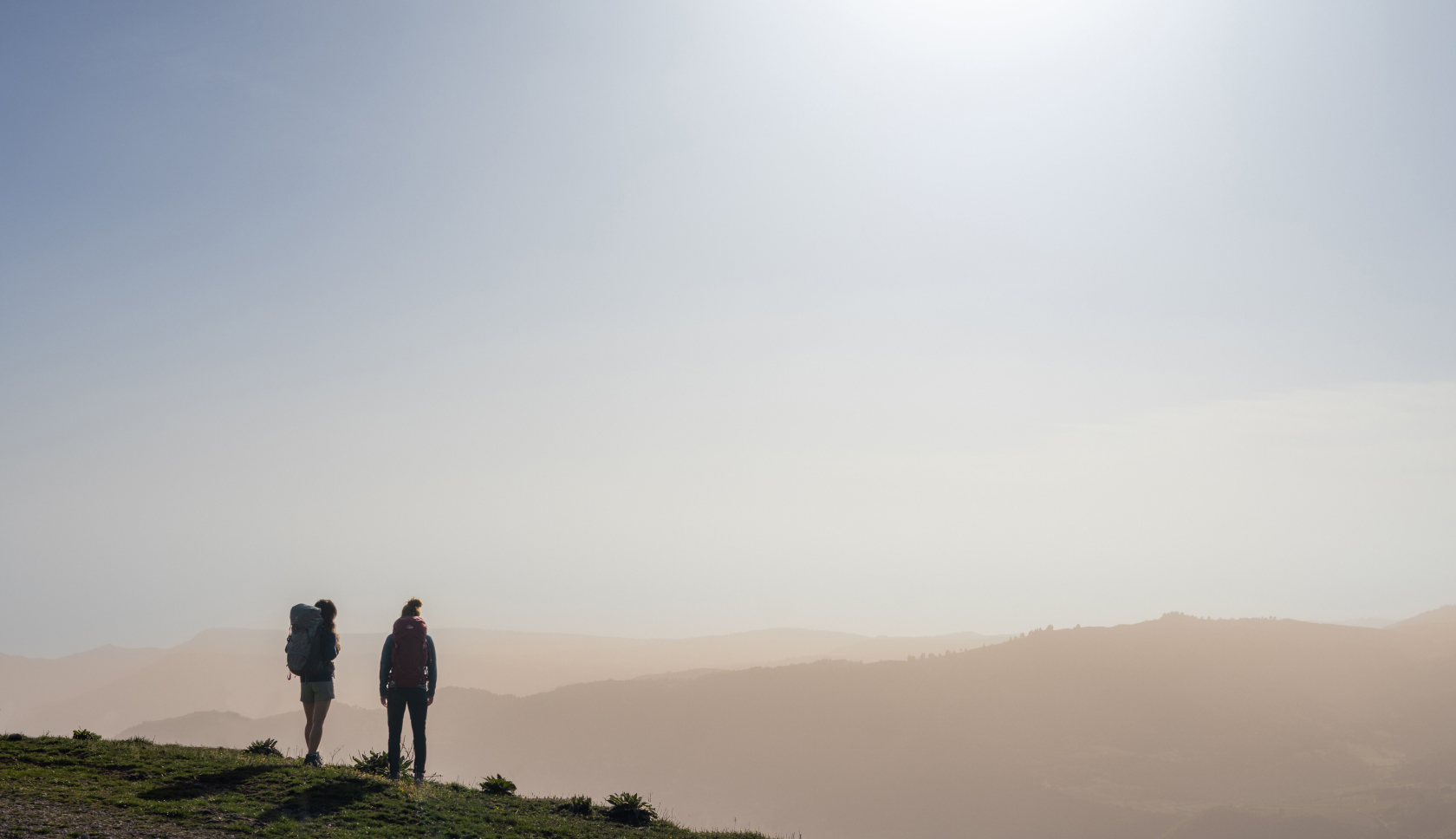 Twee personen met rugzak kijken tijdens golden hour uit over bergen