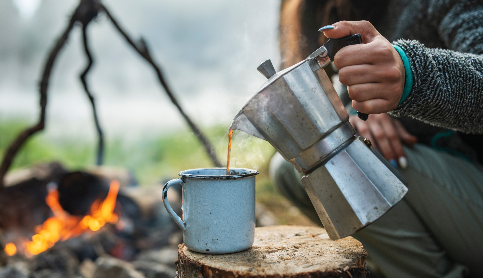 een hand schenkt koffie uit een percolator in een mok