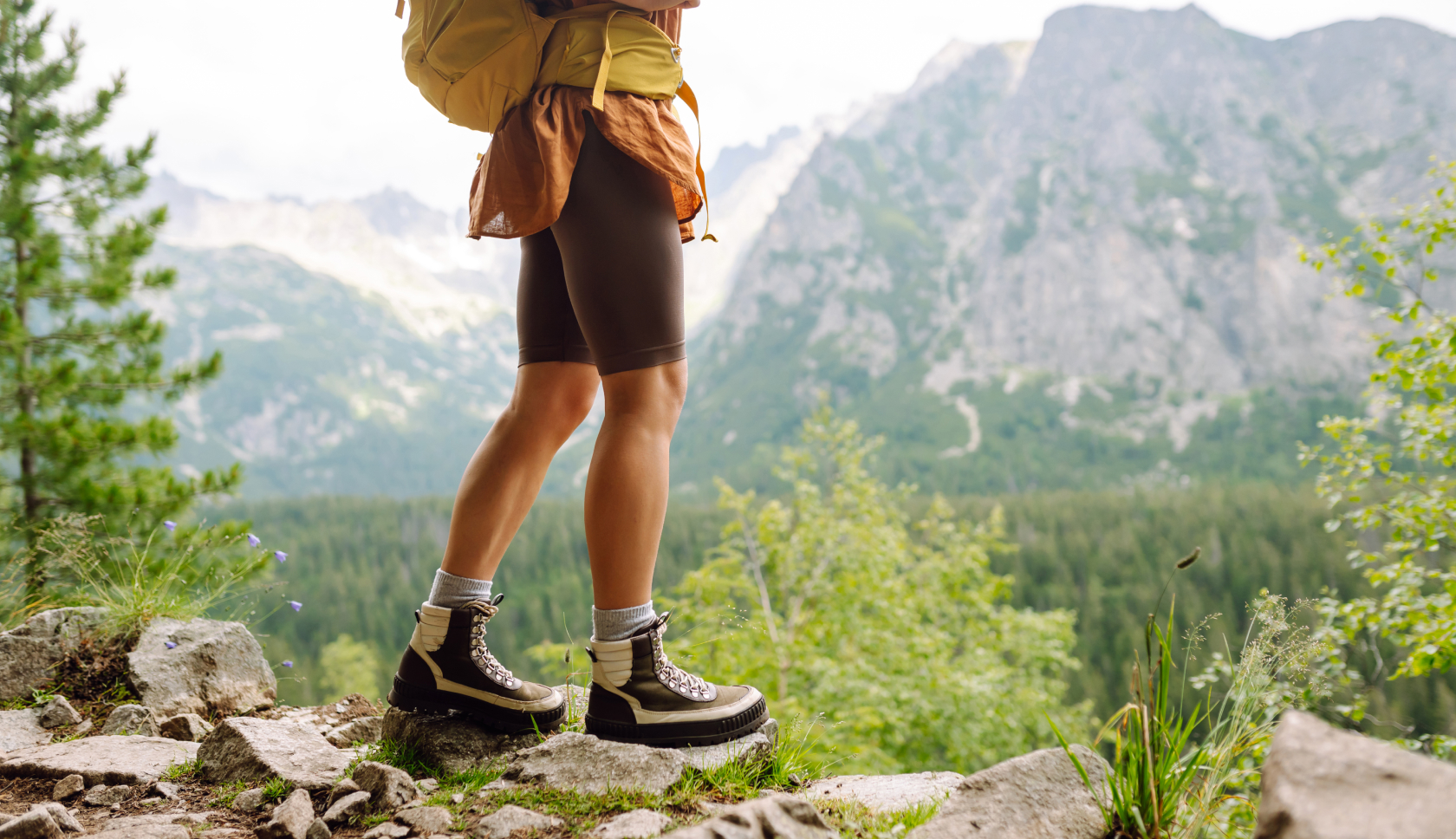 vrouw staat in haflhoge wandelschoenen op rotsig pad met bergen in de achtergrond