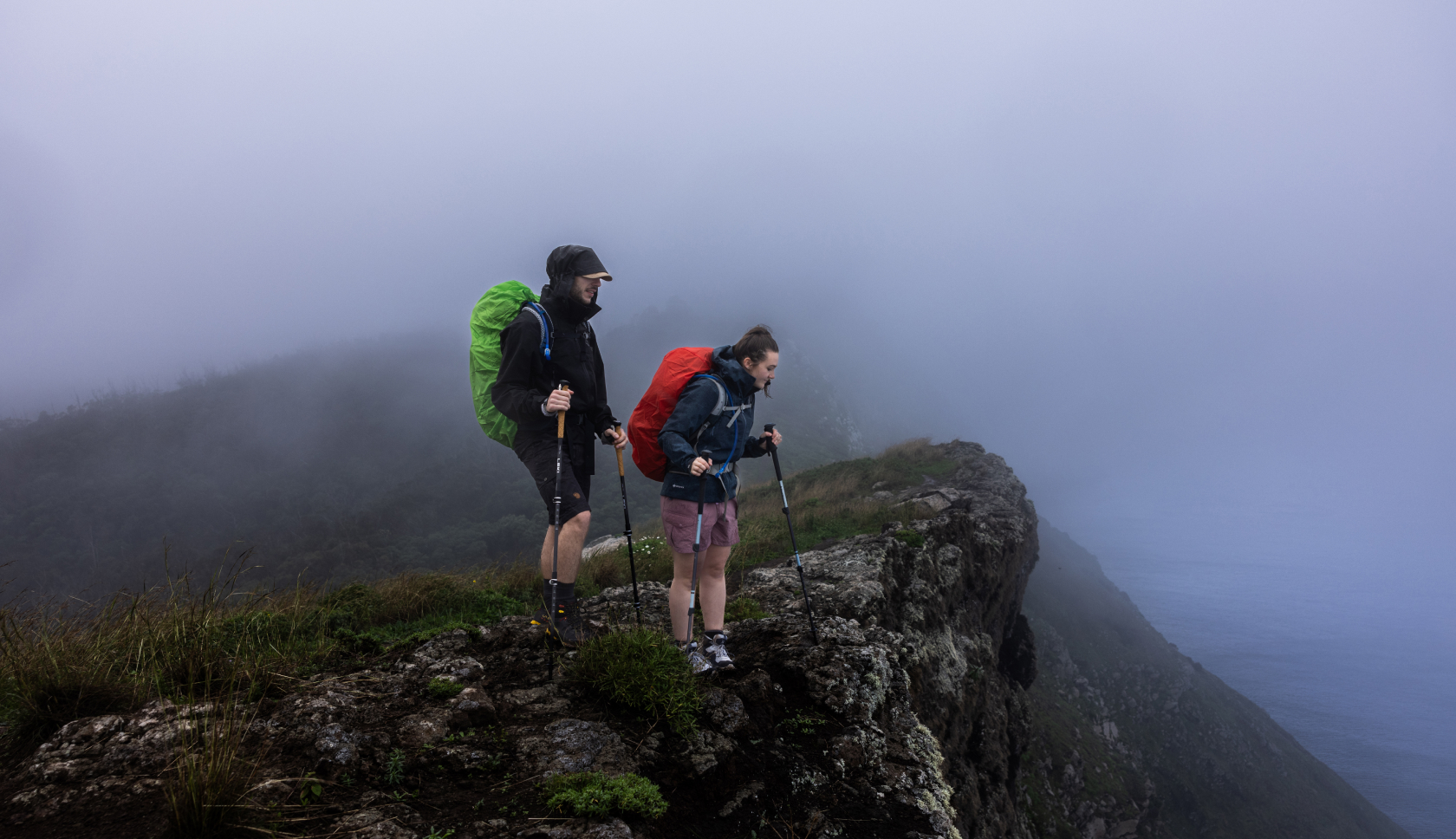 Twee personen staan in regenkleding op een bergtop.