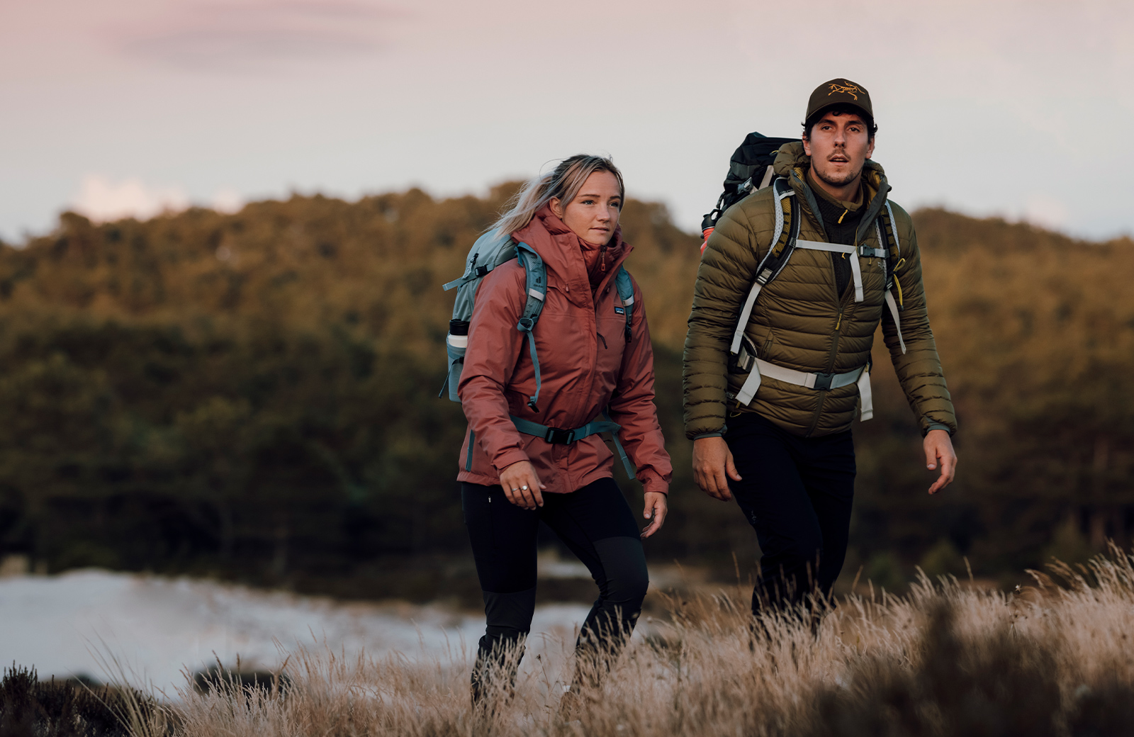 twee wandelaars lopen op een heuvel met een meer achter zich