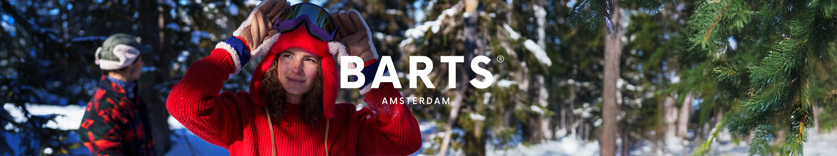 vrouw in een felrode trui en een skibril op staat in een besneeuwd bos