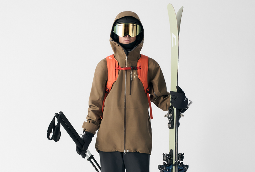 man in wintersportoutfit staat met ski's en skistokken tegen een witte achtergrond